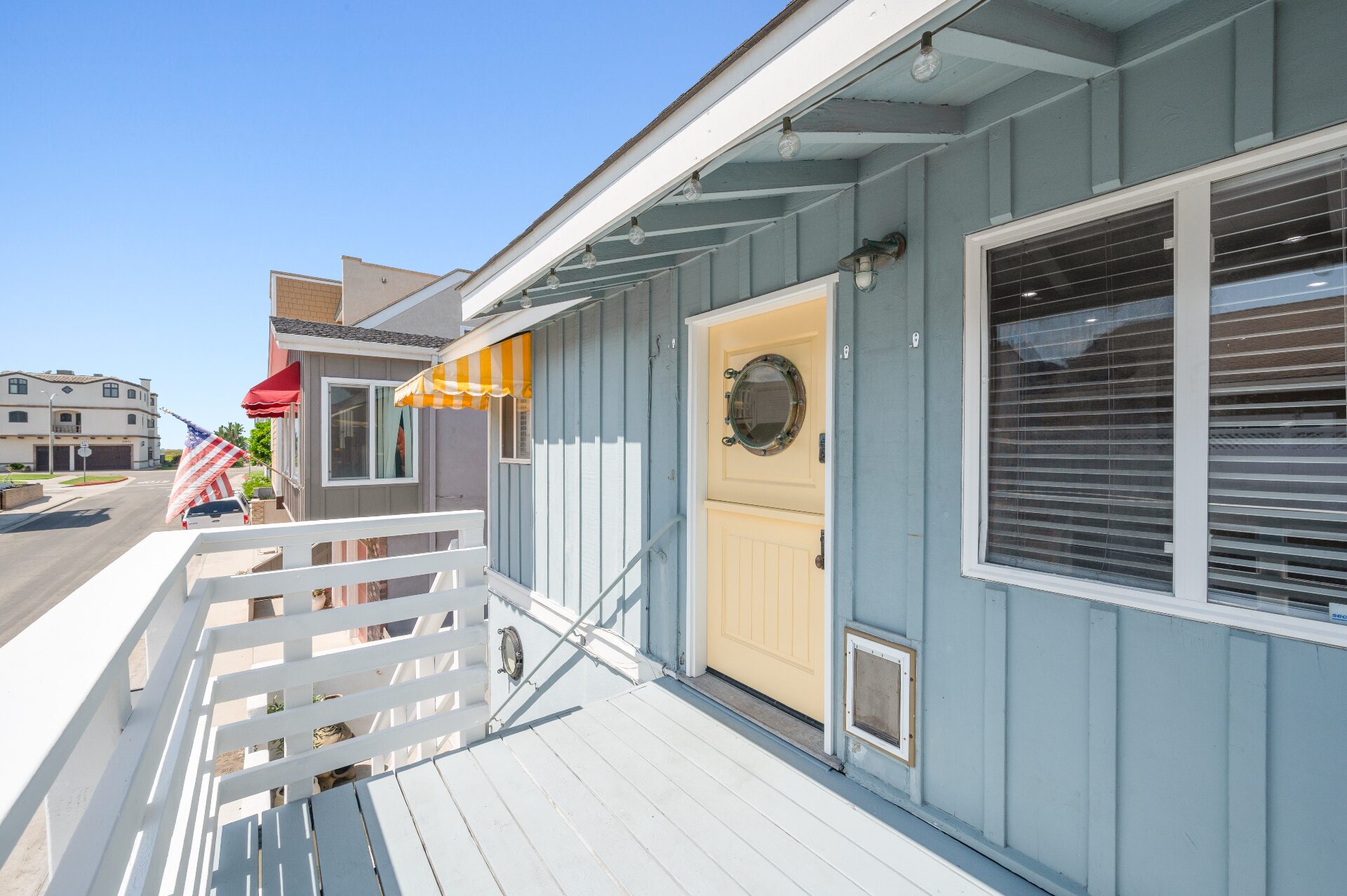 Sunny front deck and entry with nautical porthole door, striped awning, and neighborhood ocean-side setting