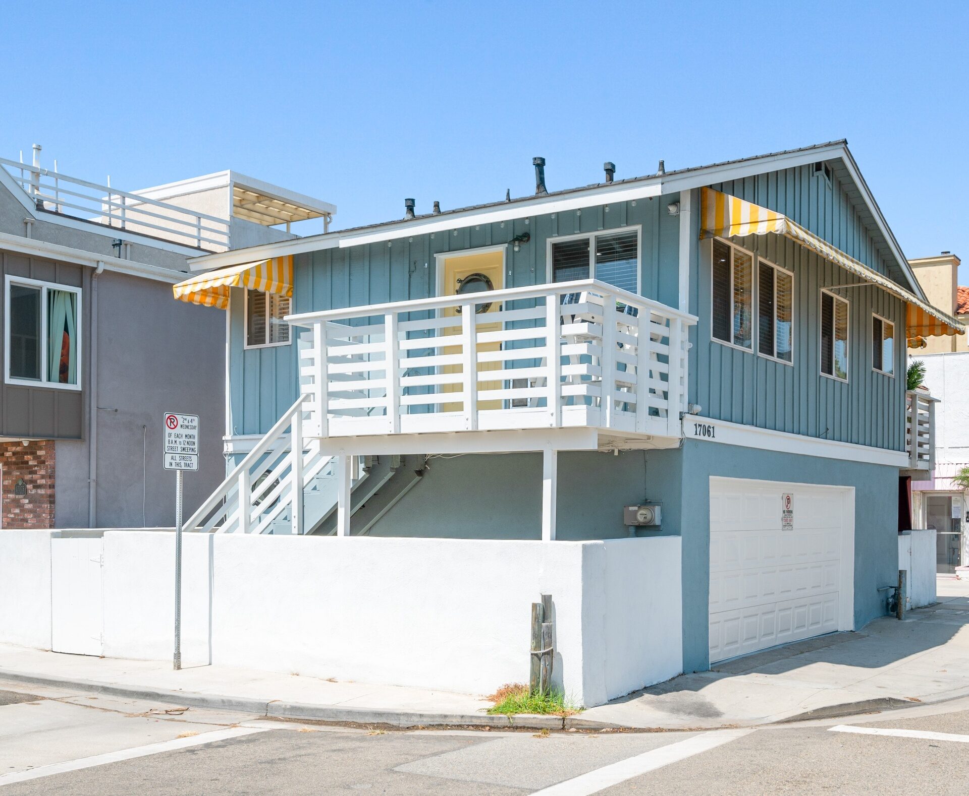 Coastal exterior with blue siding, crisp white railings, striped awnings, and beach-close curb appeal