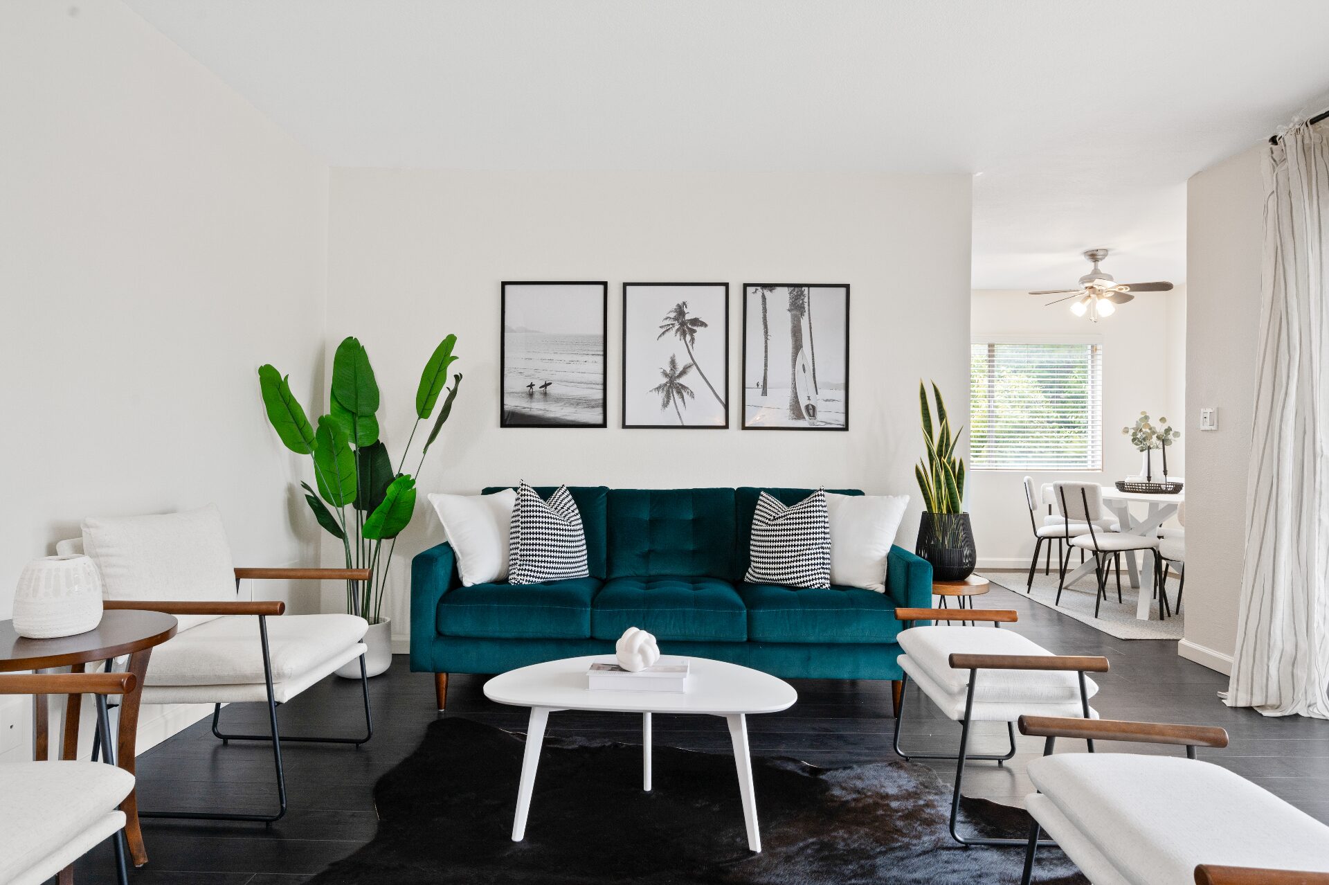 Bright staged living room with teal velvet sofa, framed coastal art, and open dining area