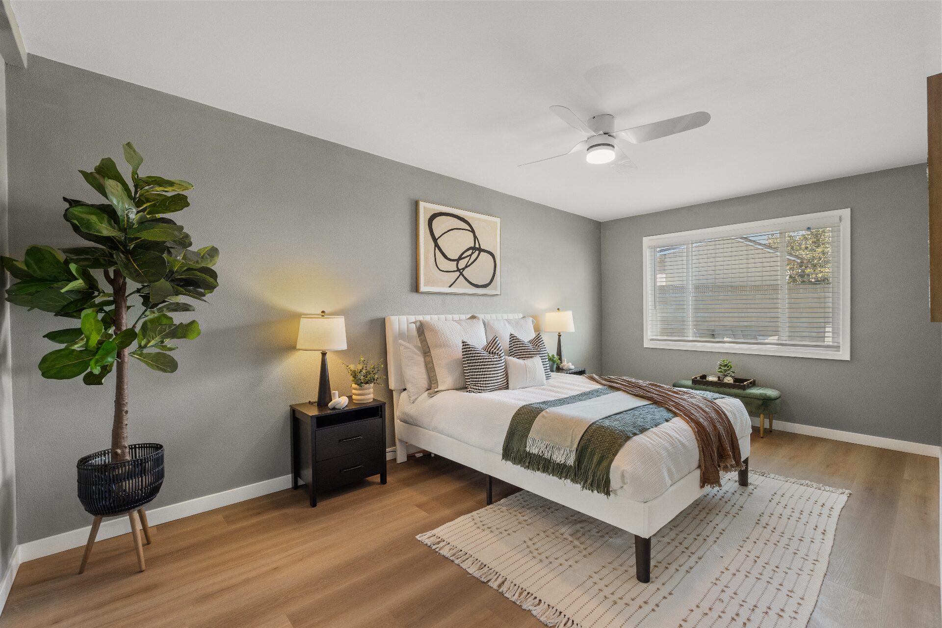 Staged primary bedroom with upholstered bed, layered throws, abstract art, and large window