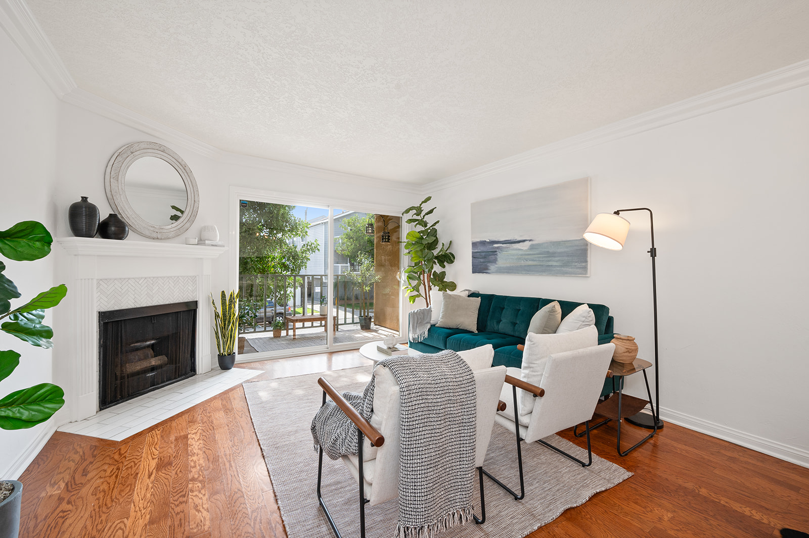 Bright living room with white fireplace, teal velvet sofa, hardwood floors, and patio sliders