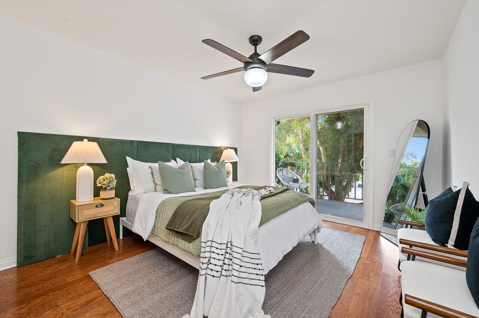 Primary bedroom with green velvet headboard, layered bedding, full-length mirror, and patio access