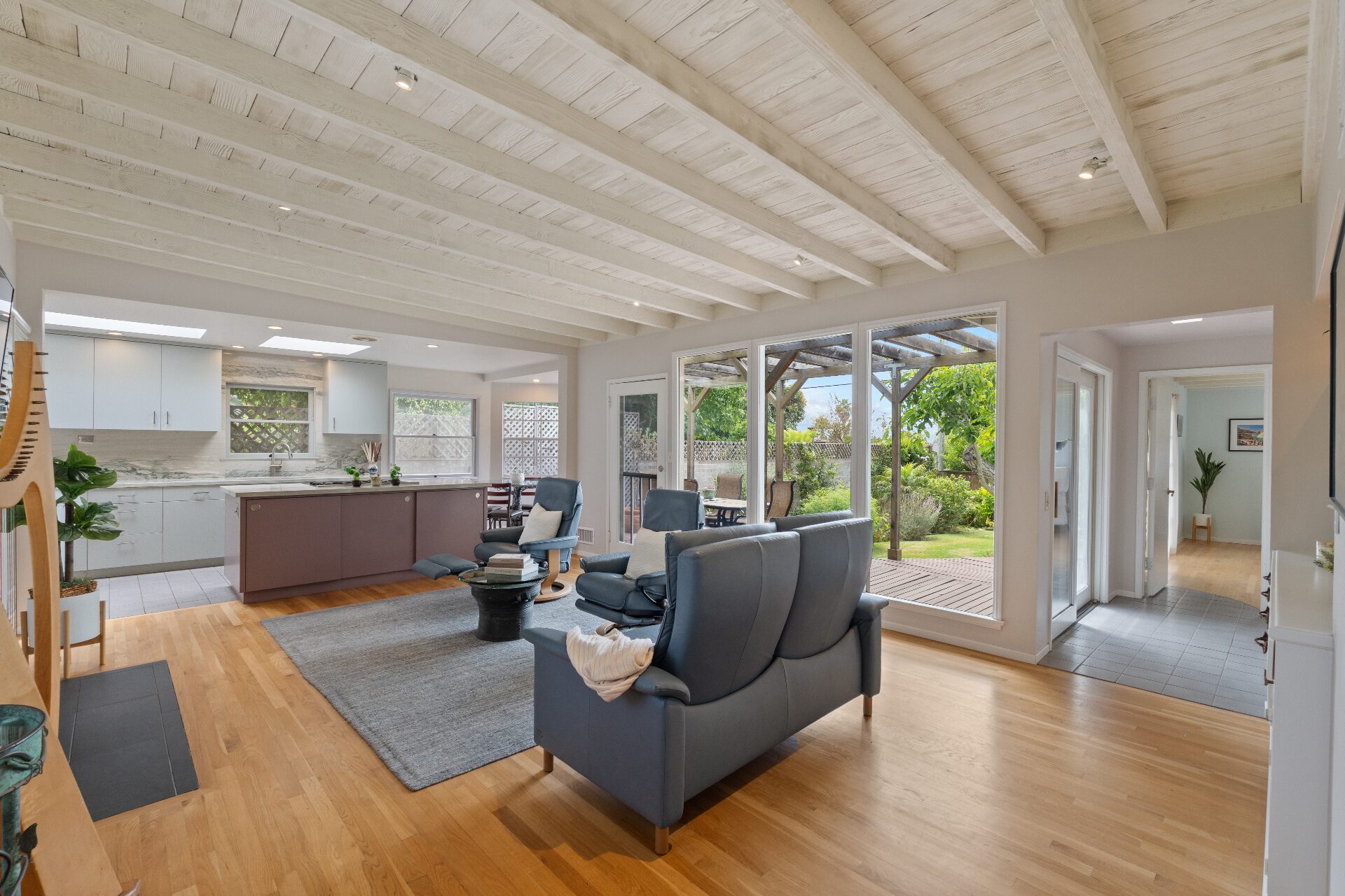Open great room with whitewashed beam ceiling, wide-plank floors, updated kitchen, and garden views through picture windows