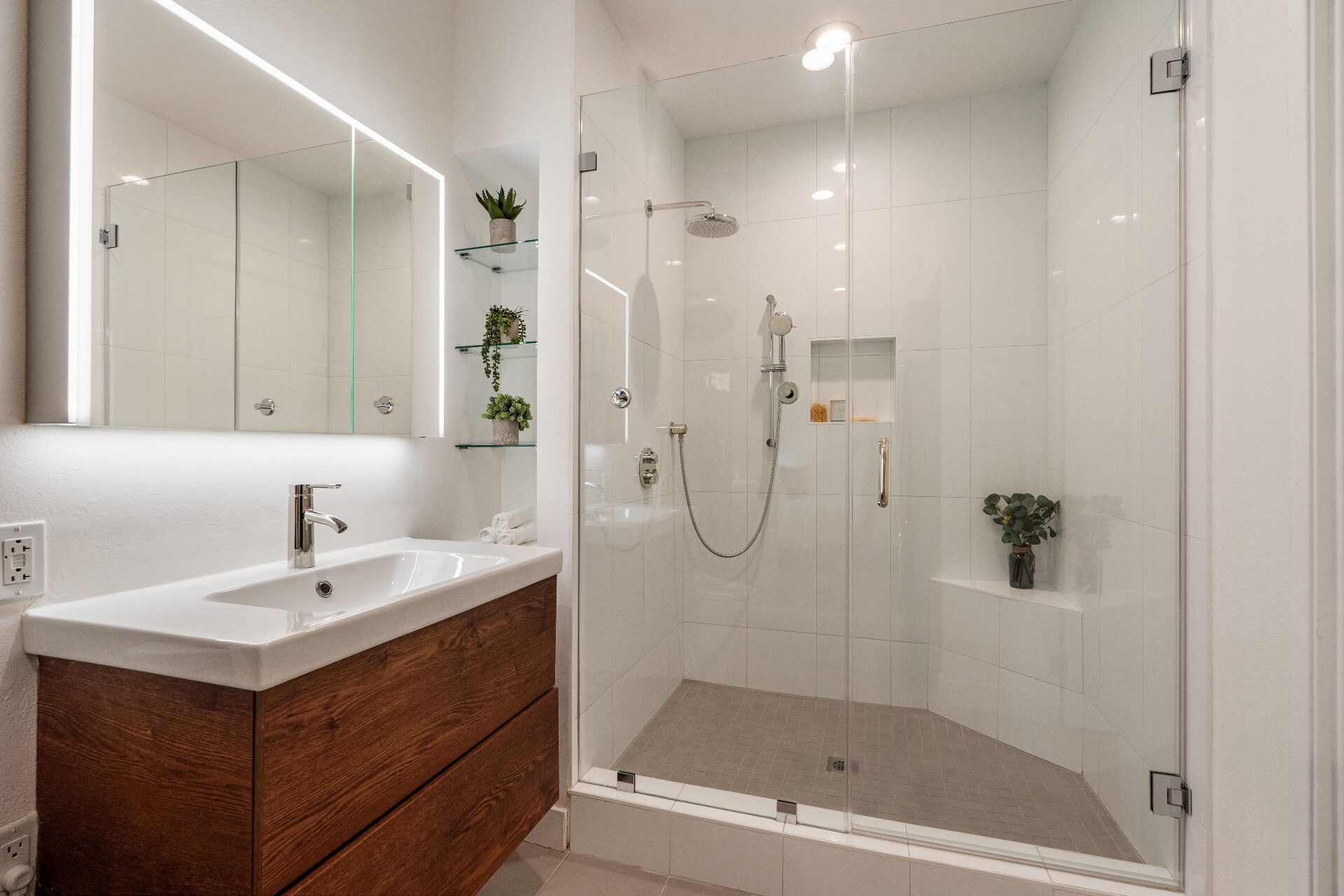 Modern spa-style bathroom with backlit mirror, walnut floating vanity, glass walk-in shower, and rainfall showerhead