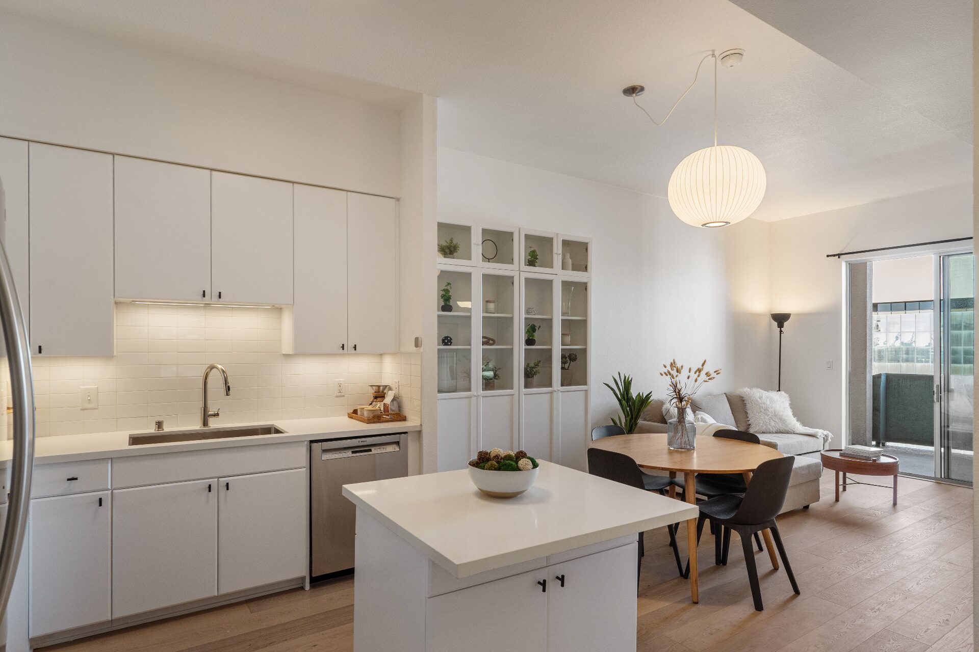 Bright modern kitchen with white cabinets, quartz island, dining nook, and ocean-view balcony beyond