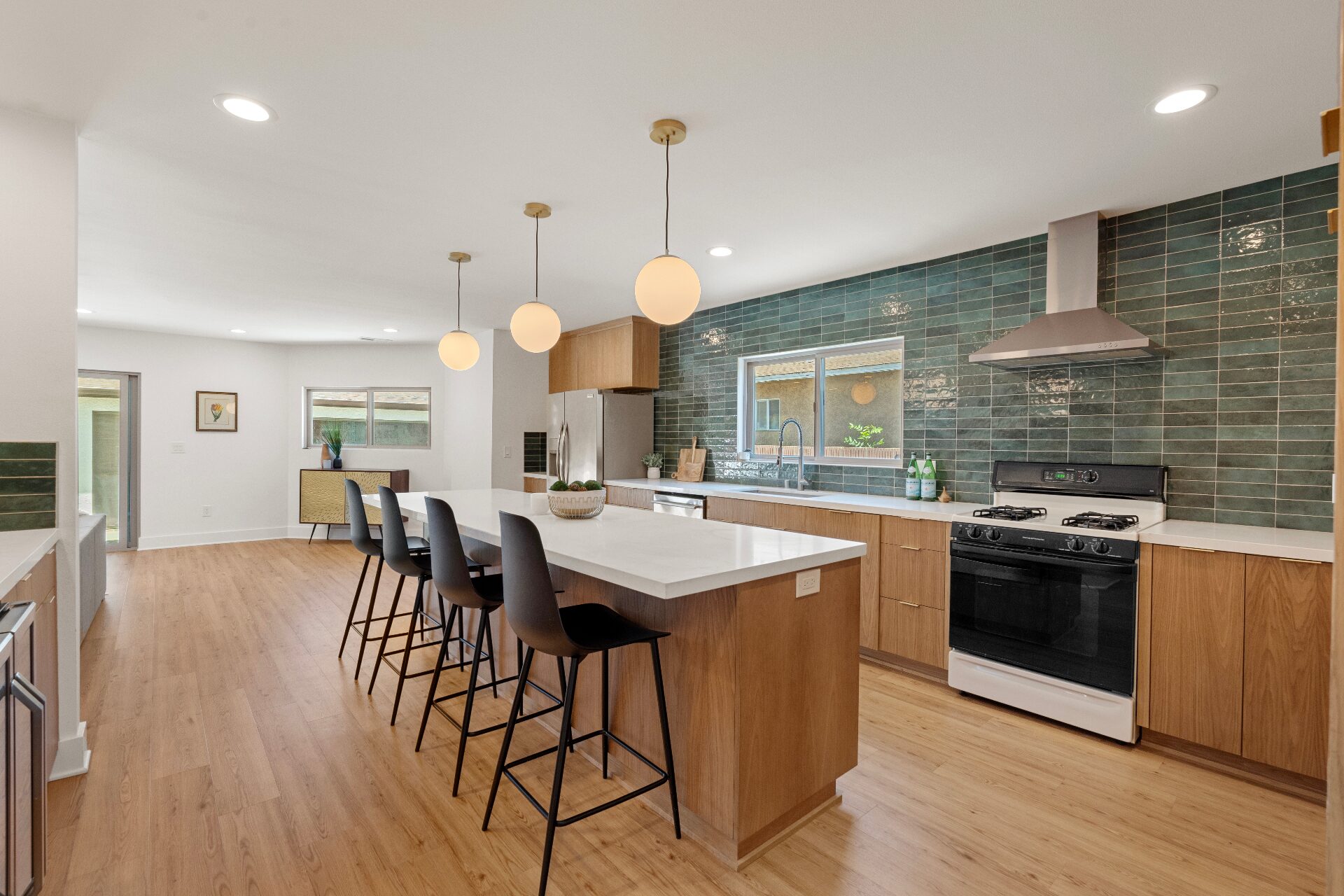 Modern kitchen with long waterfall island, warm wood cabinetry, glossy emerald tile backsplash, and globe pendants