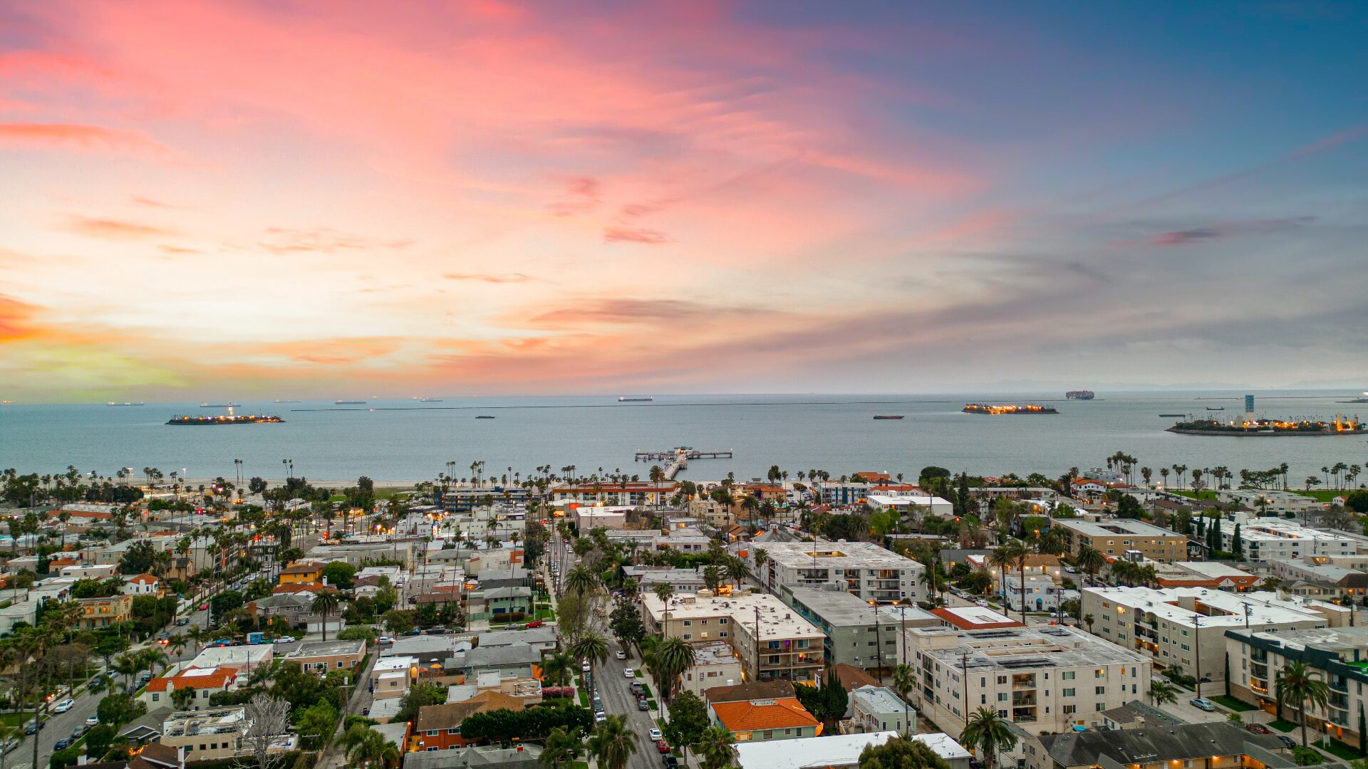 Oceanfront aerial sunset with colorful sky and palm-lined shoreline near 226 Grand Ave